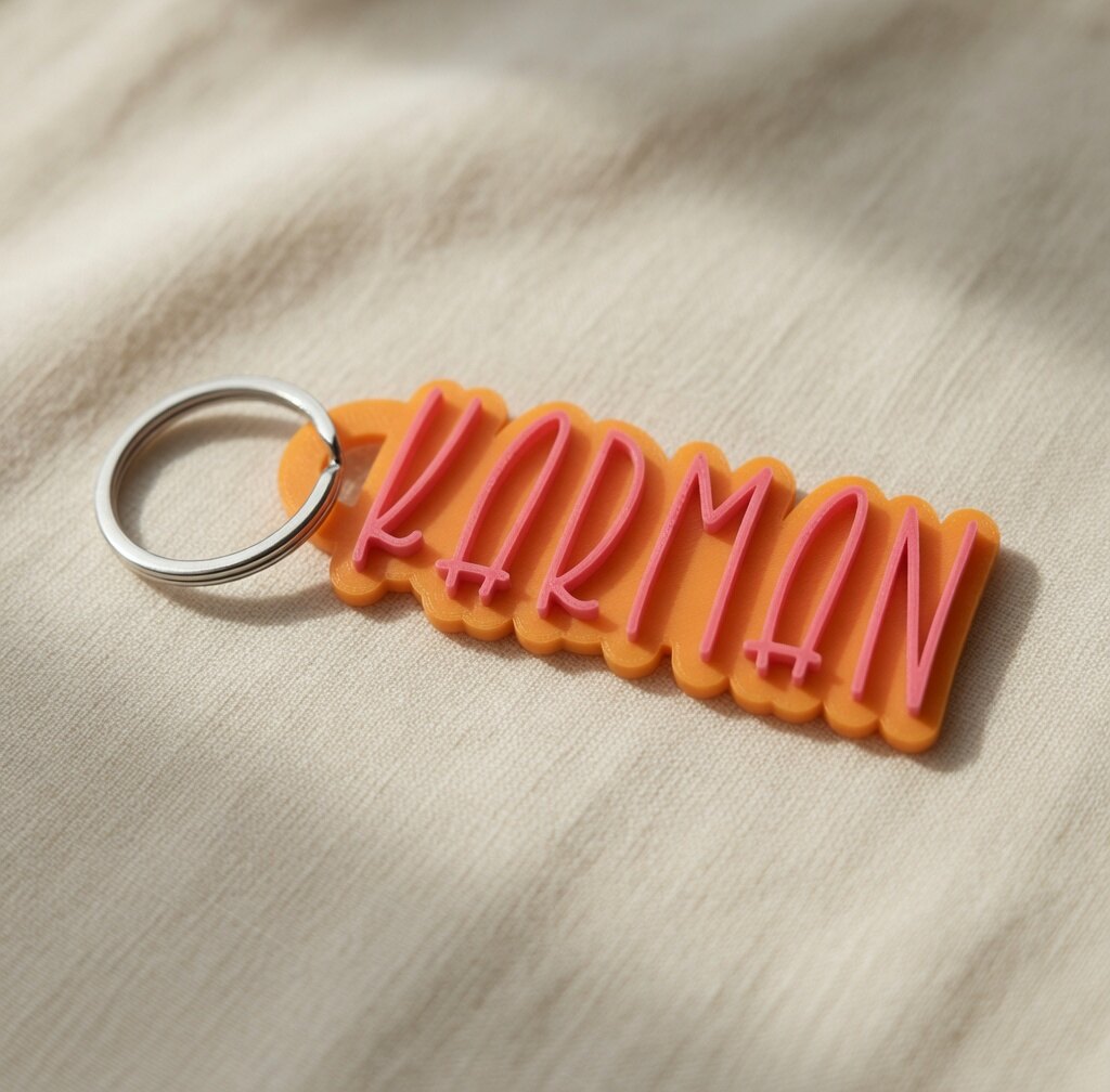 Orange 3D-printed KARMAN keychain with raised pink letters and a metal ring, on linen